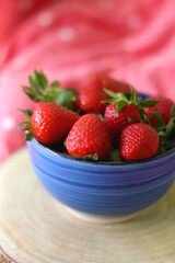 Bowl of fresh strawberries on a bed with colorful bedding. Selective focus.