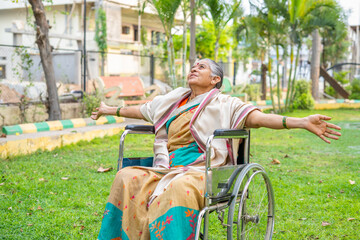 Happy senior women feeling natures fresh air by stretching arms while sitting on wheelchair at...
