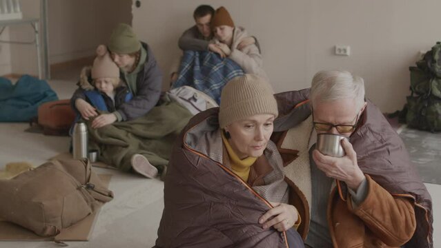 Slowmo of small group of refugee men and women living together in cold asylum, supplied with water, warm clothes and sleeping bags