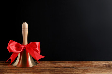 Golden bell with red bow on wooden table near blackboard, space for text. School days - obrazy, fototapety, plakaty