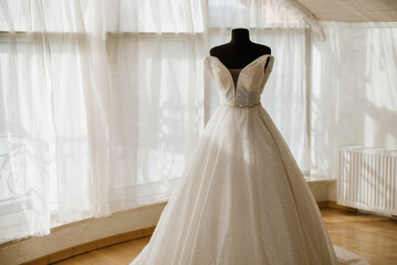 Stylish wedding dress on a mannequin in the morning by the window on the wedding day. Preparing for...