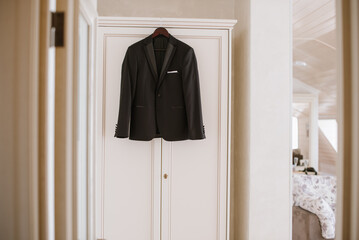 Stylish groom's jacket hangs on the closet in the morning on the wedding day - 500411498