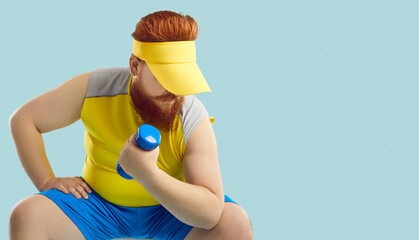 Serious fat young man is actively training with dumbbell isolated on light blue background....