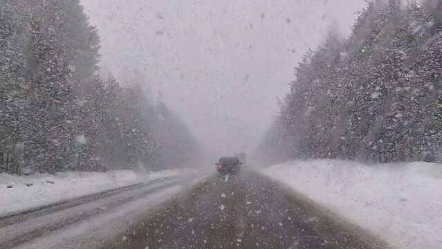 The car is driving along the highway through snow and blizzard. Video through the windshield on a winter storm.