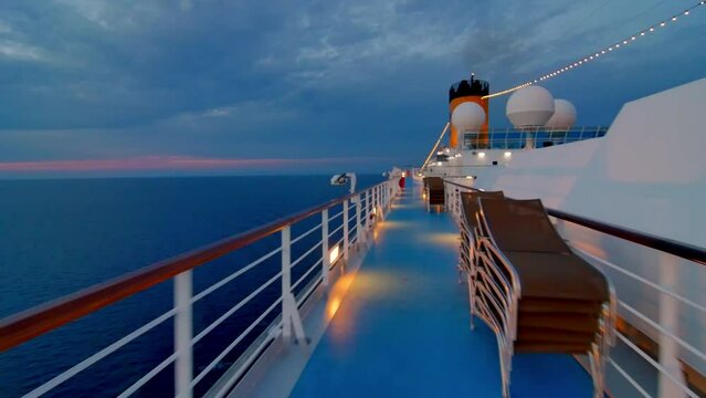 Cinematic  traveling over the deck of a large luxurious cruise ship during the splendid sunset of blue and purple colors where we see the immensity of the sea and the deck of the ship