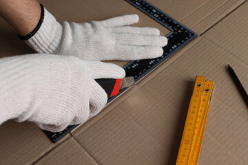Worker cutting cardboard with utility knife and ruler, closeup - obrazy, fototapety, plakaty