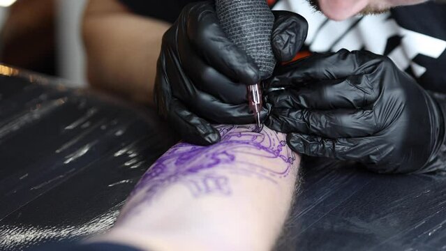 Tattoo master is tattooing a man's hand. Wireless tattoo machine, safety and hygiene at work. Close-up of tattoo artist work. Tattoo salon