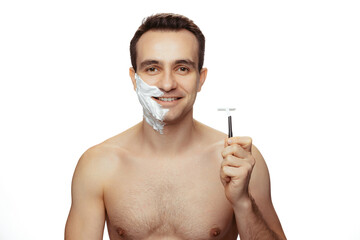 Portrait of young smiling man with half-face covered with shaving cream, holding razor isolated...