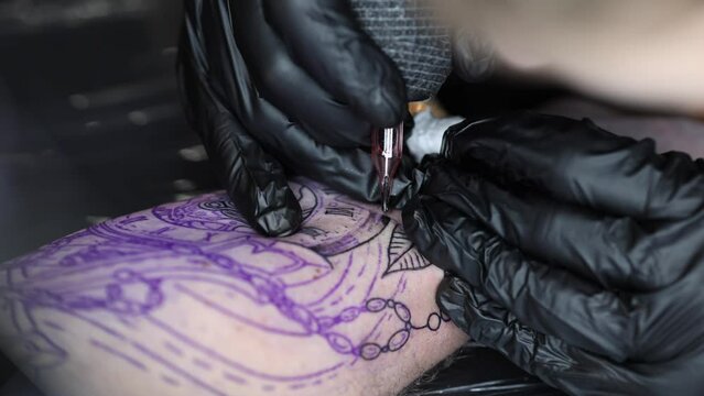 Close up of a young professional tattoo master introduces black ink into the skin using needle from a wireless tattoo machine. Tattoo on hand