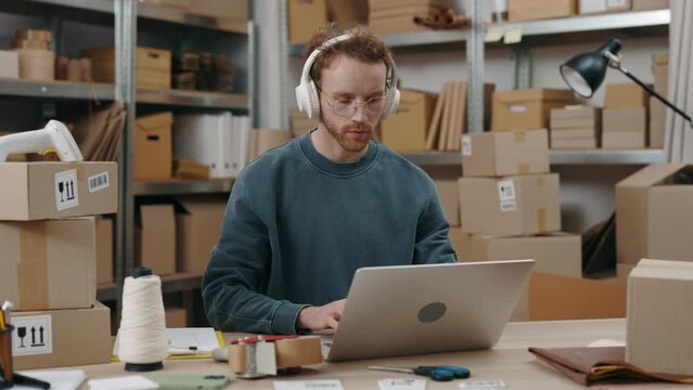 Attentive Caucasian Man Wearing Glasses Sitting At The Laptop Computer And Typing Something At The Keyboard While Working At The Home Office. Post Service And Small Business Concept.