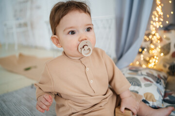 baby with a pacifier in his mouth sits on the floor