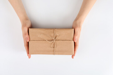 Woman holding parcel wrapped in kraft paper on white background, top view