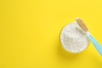 Bowl of tooth powder and brush on yellow background, flat lay. Space for text