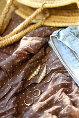 Brown polka dot blouse, vintage mom jeans, straw bag, round sunglasses, gold rings and pearl hair clips. Fashionable outfit on wooden background. Selective focus.