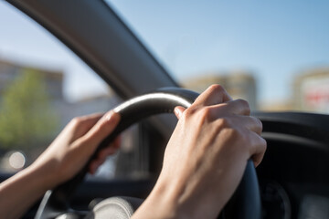 Hands of the female driver on the steering wheel of the car. Traffic control in motion, close-up
