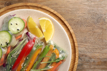 Delicious rolls wrapped in rice paper on wooden table, top view. Space for text