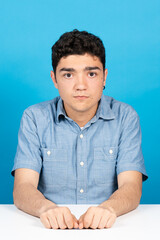 Serious hispanic teenager boy looking at camera isolated on blue background.