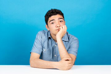 Webcam view of bored hispanic teenager looking at camera isolated on blue background.