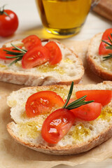 Fototapeta na wymiar Tasty bruschettas with oil, tomatoes and rosemary on parchment paper, closeup