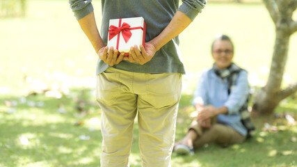 Naklejka premium Asian Lifestyle senior couple surprise gift for special day in the nature park happy and relax time. Elderly family the rest and chill after retirement in vacations.