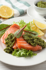 Tasty cooked salmon with pesto sauce served on white wooden table, closeup