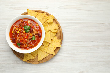 Bowl with tasty chili con carne and nachos on white wooden table, top view. Space for text