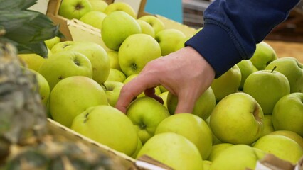 A man in the market chooses fresh fruits, the buyer chooses green apples on the store shelf. Buying fresh fruit for a healthy diet. Beautiful and juicy apples on the store shelf