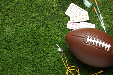 American football ball, whistle and different drugs on green grass, above view with space for text....
