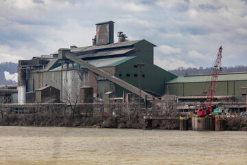 Obraz premium Large green factory building on edge of river