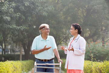 Female physical therapist discussing with senior man in wheelchair at park