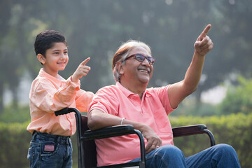 Little grandson pushing disabled grandfather on wheelchair at park