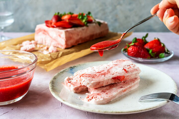 Italian strawberry dessert Semifreddo on plate with human hand holding teaspoon with strawberry's...
