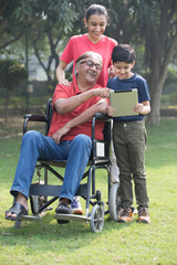 Happy grandfather in a wheelchair check a digital tablet with granddaughter at park