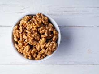 Peeled walnuts in a bowl on a white wooden background. Top view