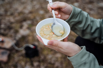 Pea soup with breadcrumbs in a plate, hold a cup with food with your hands, eat food with a spoon on a hike, a tourist's lunch is filmed close-up, a quick meal, a light breakfast.