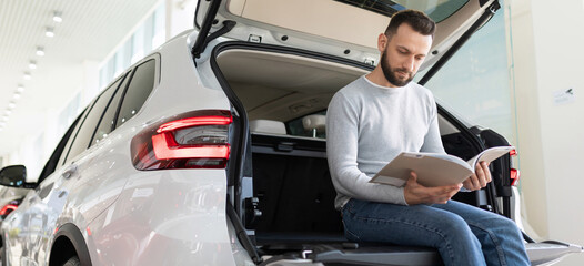 A man sits in the trunk of a car looking at an insurance offer