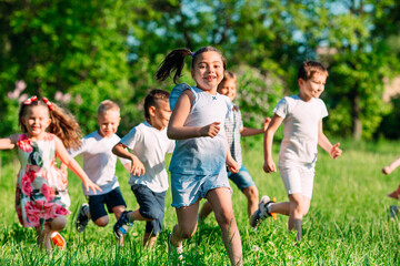 A group of happy children of boys and girls run in the Park on the grass on a Sunny summer day.