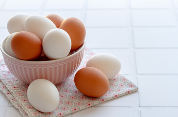 Raw white and brown eggs in pink bowl on white ceramic pile background.  Image is about kitchen interior design, morning routine, homemade receipe/ Healthy organic food concept.