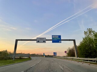 Italian highway with road sign indicating Milano Malpensa airport at sunrise.
