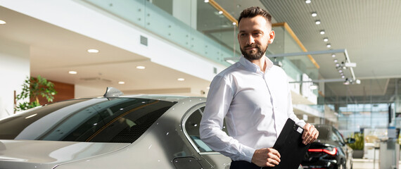 presentable insurance agent next to a new sedan in a car dealership