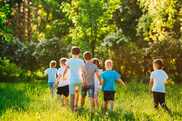Fototapeta premium A group of happy children of boys and girls run in the Park on the grass on a Sunny summer day.