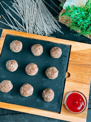Raw Meatballs on a cutting board with greens.