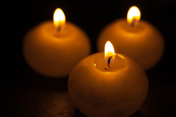 Obraz na płótnie Canvas Burning bright golden candles on black background. Festive or mourning candles.