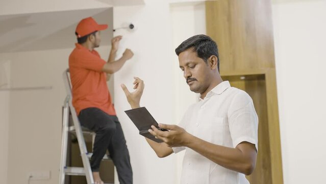technician fixing angle or view of cctv camera while customer or owner checking in digital tablet at home - concept of employment, blue caller jobs and surveillance technology