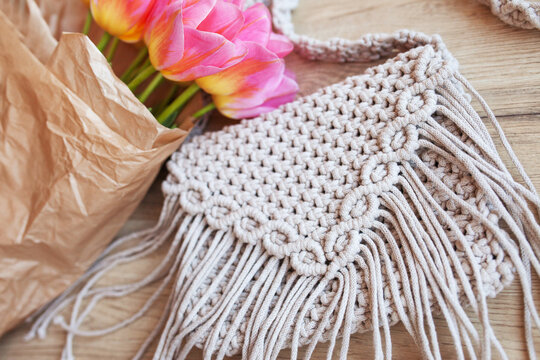 Handmade macrame cotton сross-body bag. Eco bag for women from cotton rope  with bouquet of flowers in kraft paper. Scandinavian style bag. Beige  tones, sustainable fashion accessories. Close up image Stock Photo