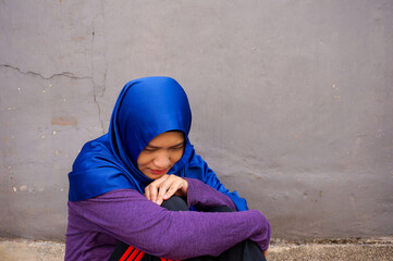 Lonely and depressed young muslim woman sitting in a street. Stress exhausted feeling down...