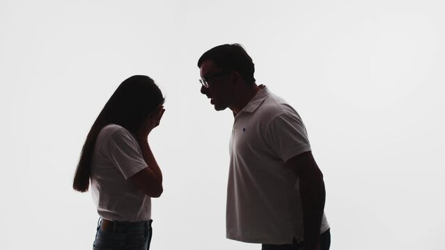 Silhouette of married couple, man yelling at woman, she covers face with hands, white background in studio. Husband screams and gets angry at wife. Concept of abuse