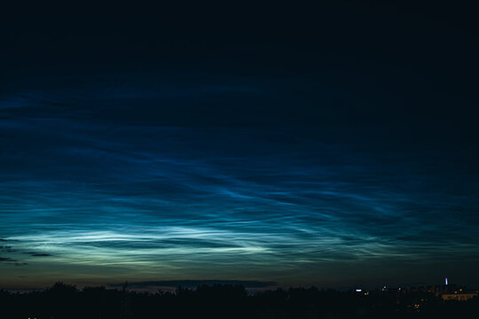 Noctilucent mesospheric clouds in night sky. Rare atmospheric phenomenon over city.