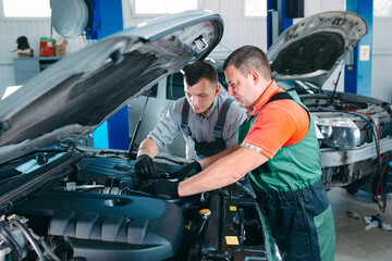 Two handsome mechanics in uniform are working in auto service. Car repair and maintenance.