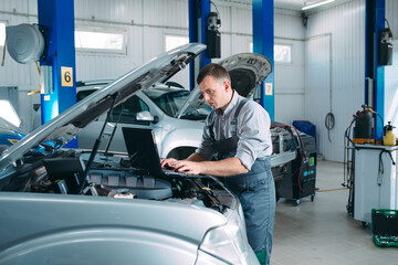 car mechanic using a computer laptop to diagnosing and checking up on car engines parts for fixing and repair.